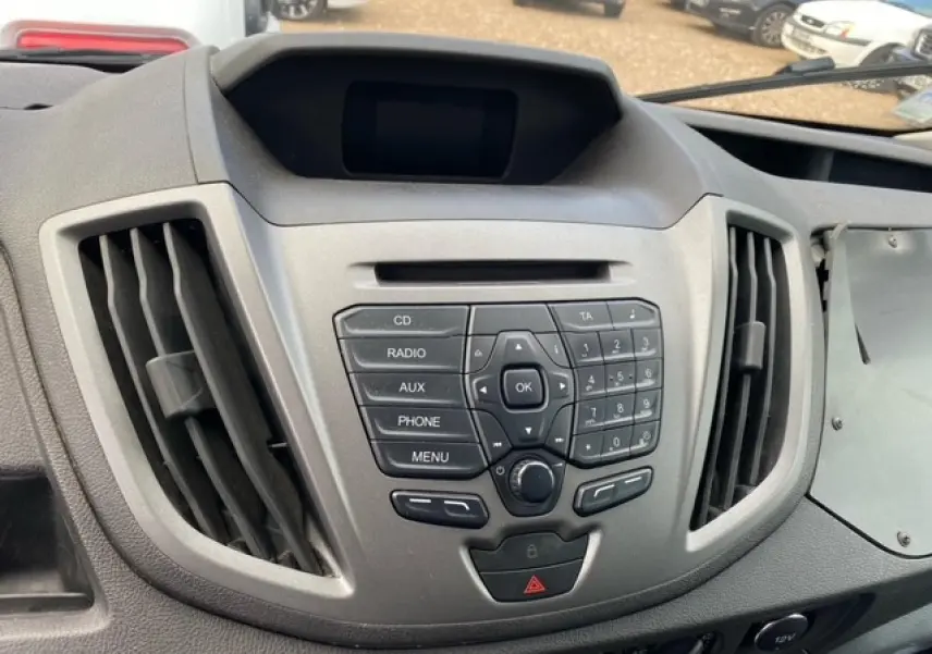 Vue rapprochée du tableau de bord gris du Ford Transit Fourgon 2015 avec commandes audio et aérateurs centraux.