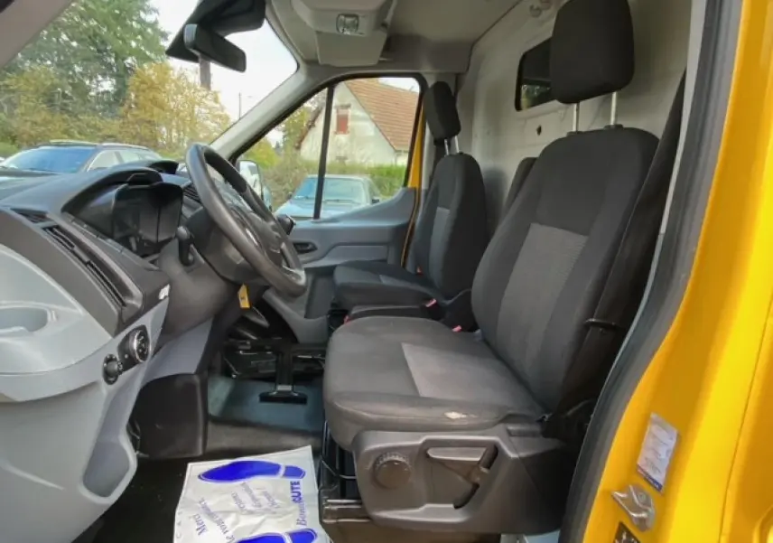Vue intérieure côté conducteur du Ford Transit Fourgon orange, montrant les sièges avant et le tableau de bord.