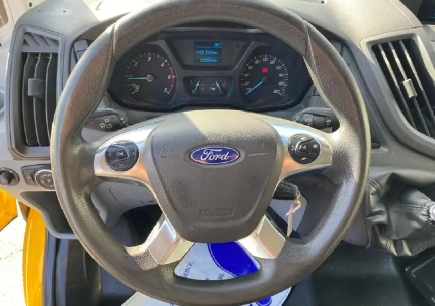 Vue rapprochée du volant Ford noir avec commandes intégrées, tableau de bord et levier de vitesse du Transit Fourgon orange 2015.