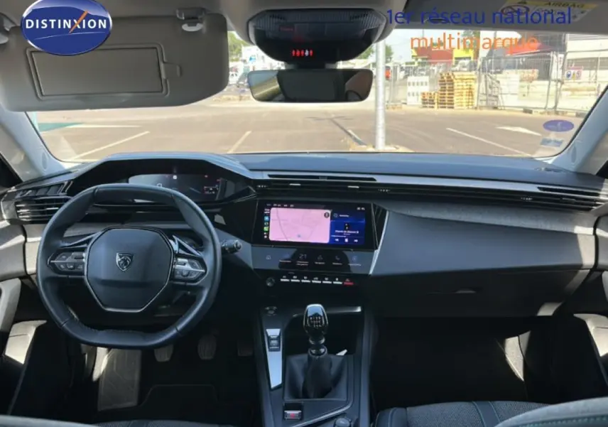 Vue intérieure frontale du poste de conduite de la Peugeot 308 bleu clair, avec volant compact, écran tactile et levier de vitesses manuel.