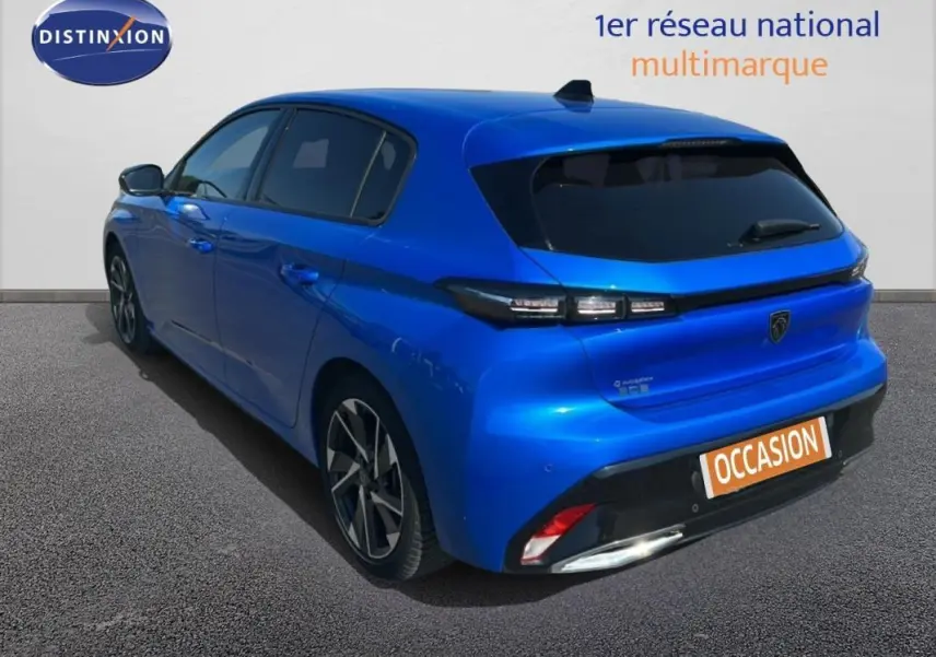 Vue 3/4 arrière gauche d'une Peugeot 308 bleu clair avec jantes alliage et vitres teintées, stationnée sur sol gris.