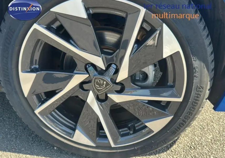 Gros plan sur la jante alliage 17 pouces noire et argentée d'une Peugeot 308 bleu clair, avec logo Peugeot central.