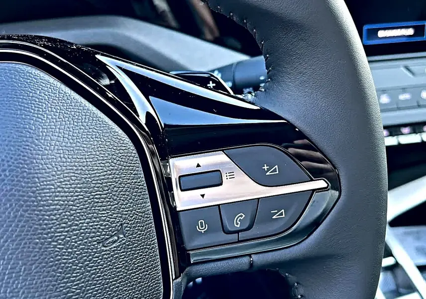 Gros plan sur les commandes multifonctions noires et argent du volant de la Peugeot 308 SW 2025 noir.