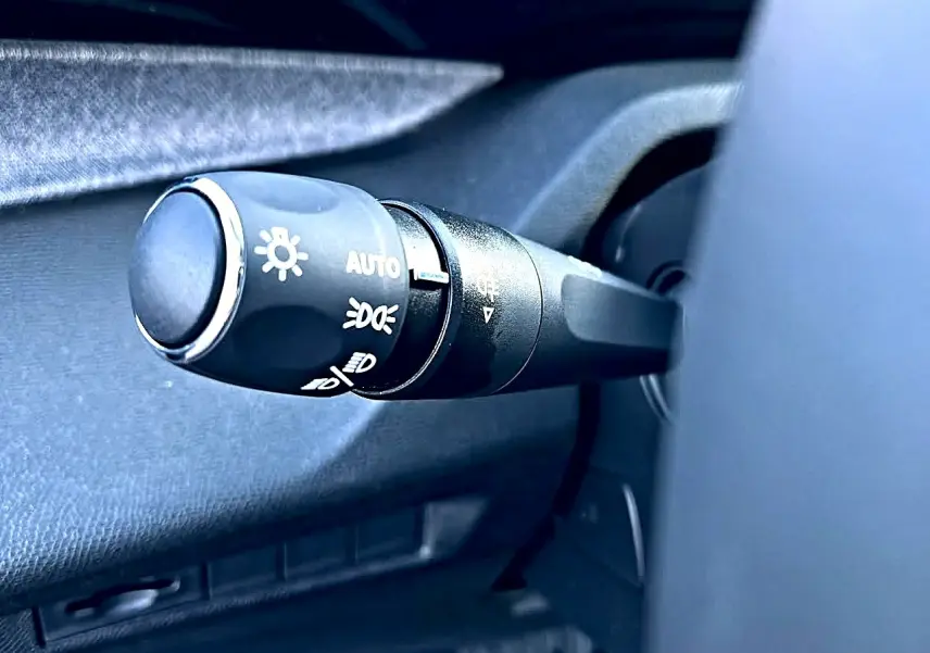 Gros plan sur la commande des phares noire à gauche du volant dans l’habitacle d’une Peugeot 308 SW noire.