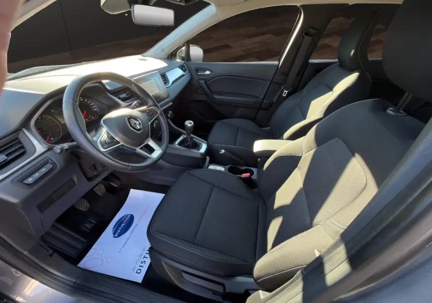 Vue intérieure côté conducteur du Renault Captur gris foncé 2024, montrant le volant cuir, tableau de bord et sièges tissu noirs.