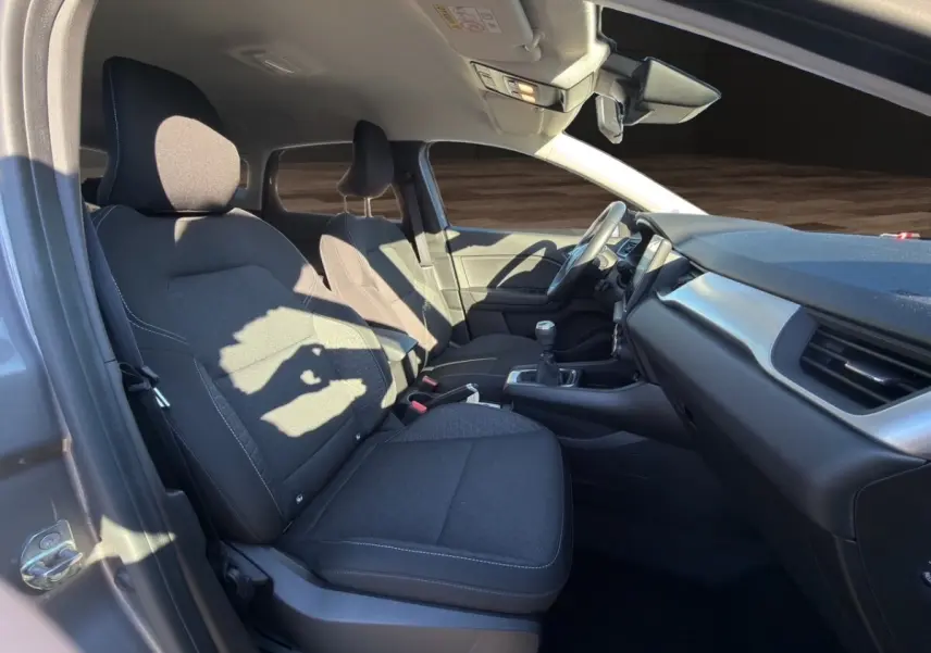 Intérieur avant droit du Renault Captur gris foncé 2024, sièges tissu noirs et tableau de bord moderne avec boîte manuelle.