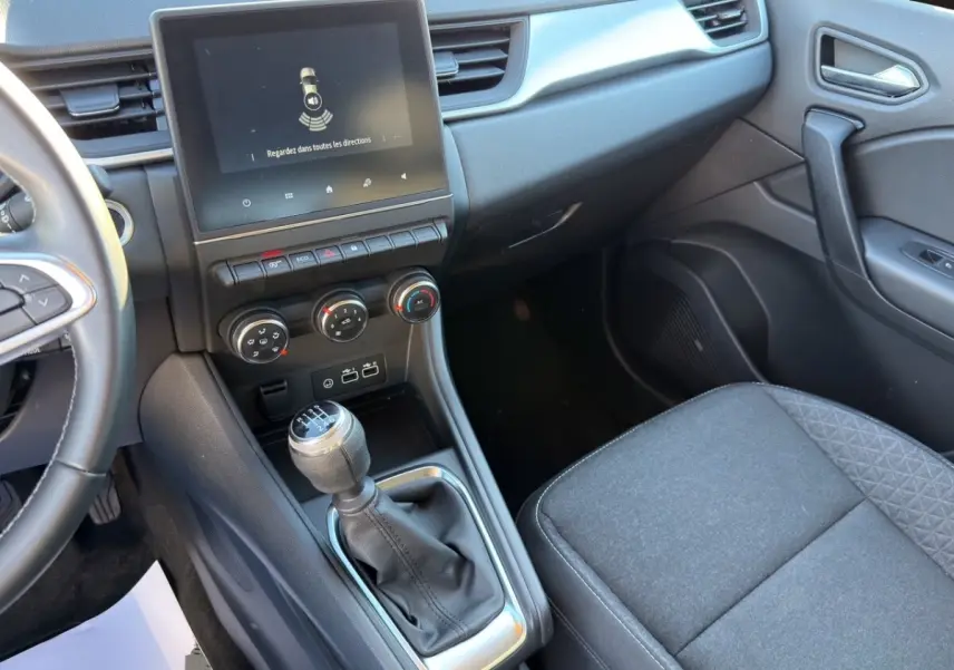 Vue intérieure côté passager du Renault Captur gris foncé 2024, avec écran tactile central et levier de vitesse manuel.