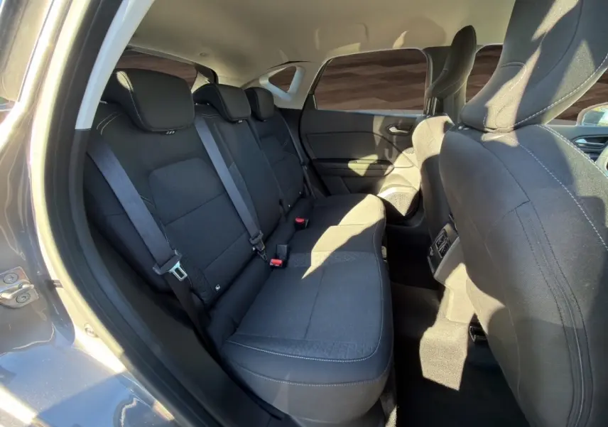 Vue intérieure côté arrière droit du Renault Captur gris foncé 2024, montrant la banquette arrière et les sièges avant en tissu noir.