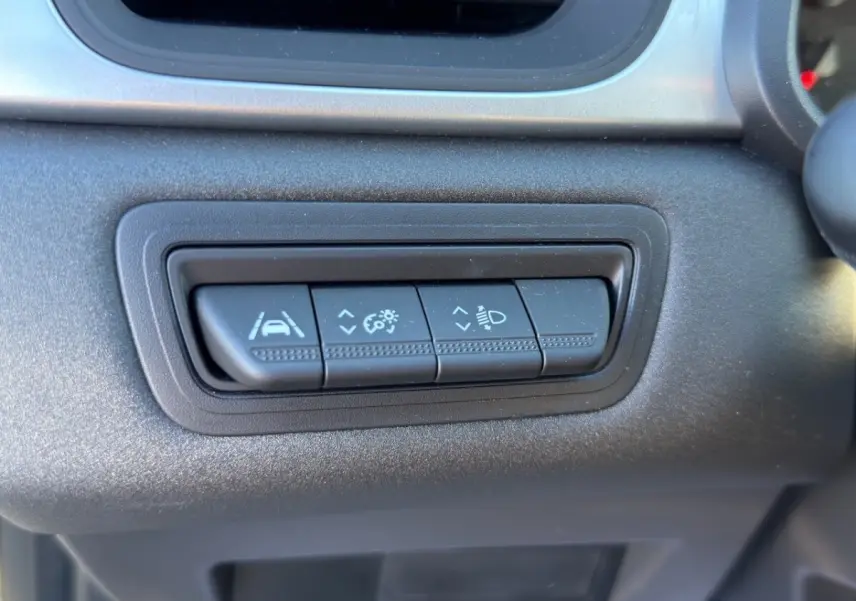 Gros plan sur les boutons de réglage des aides à la conduite et des phares du tableau de bord d’un Renault Captur gris foncé 2024.