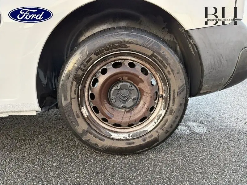 Gros plan sur la roue arrière droite rouillée d'un Citroën Berlingo blanc, montrant la jante acier et le pneu usé.