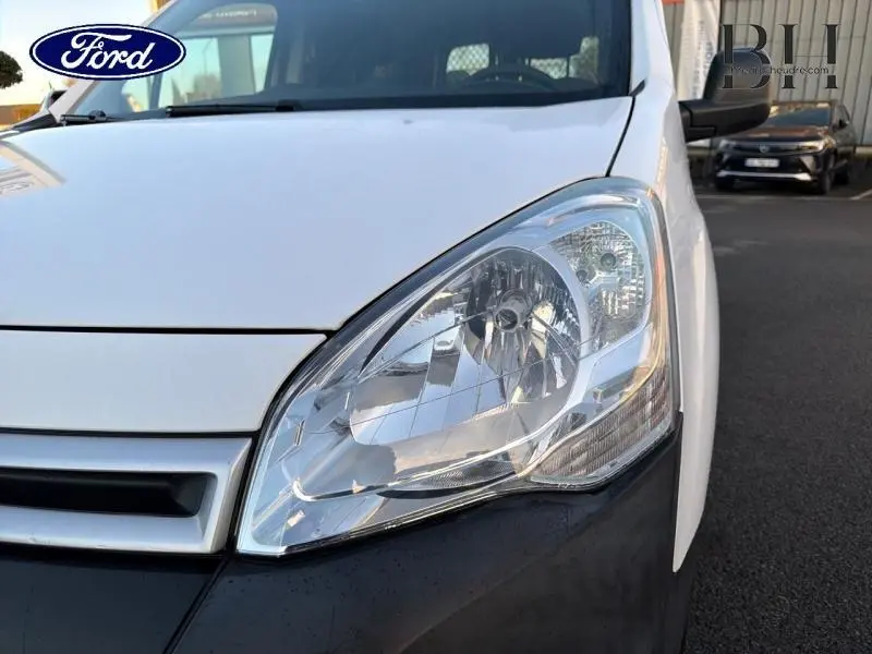Gros plan sur le phare avant droit d’un Citroën Berlingo blanc, mettant en valeur la calandre et la carrosserie.