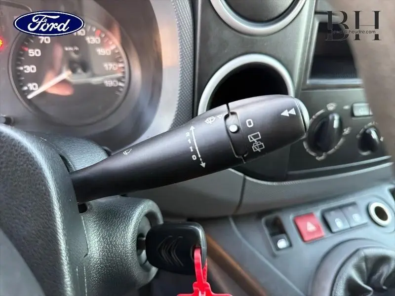 Gros plan sur le commodo d’essuie-glace dans l’habitacle d’un Citroën Berlingo blanc, avec tableau de bord et clé insérée.