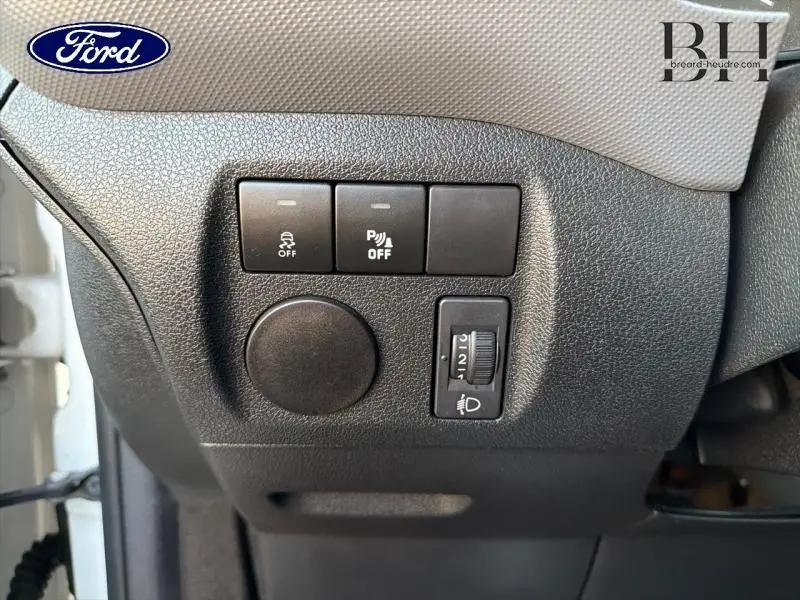 Gros plan sur les commandes de réglage des phares et aide au stationnement du tableau de bord d’un Citroën Berlingo blanc.