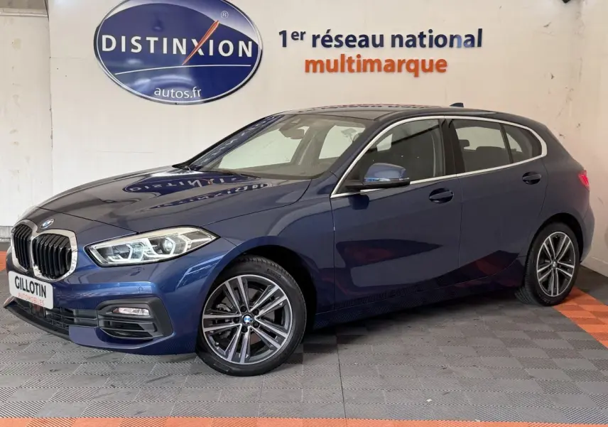 BMW Série 1 116i Business Design bleu vue 3/4 avant droit, avec jantes alliage et phares LED ellipsoïdaux.