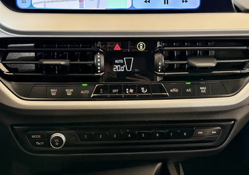 Gros plan sur la console centrale de la BMW Série 1 116i Business Design 2023, avec commandes climatisation et écran tactile visible.