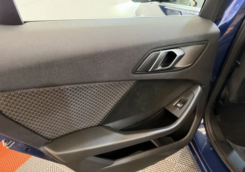 Gros plan sur la porte arrière droite bleu de la BMW Série 1 116i 2023 avec habillage tissu et commande de vitre noire.