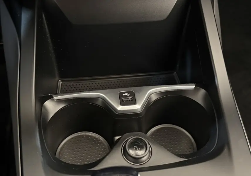 Gros plan sur les porte-gobelets noirs avec prise USB et allume-cigare dans la console centrale d'une BMW Série 1 116i.