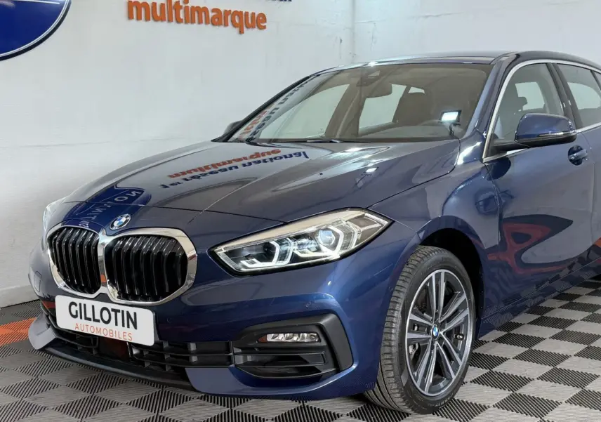 BMW Série 1 116i bleu vue 3/4 avant droit, mettant en valeur ses phares LED et calandre chromée.