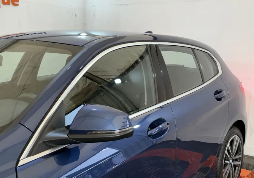 Vue côté gauche arrière d’une BMW Série 1 116i Business Design bleu avec rétroviseur et jantes visibles.
