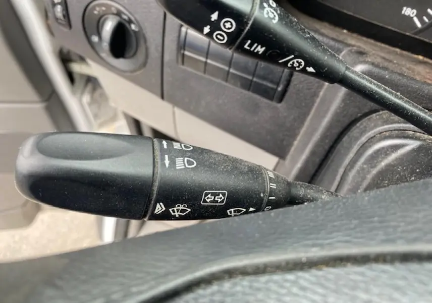 Gros plan sur les commandes de régulateur et limiteur de vitesse du Mercedes Sprinter Fourgon blanc, intérieur côté conducteur.
