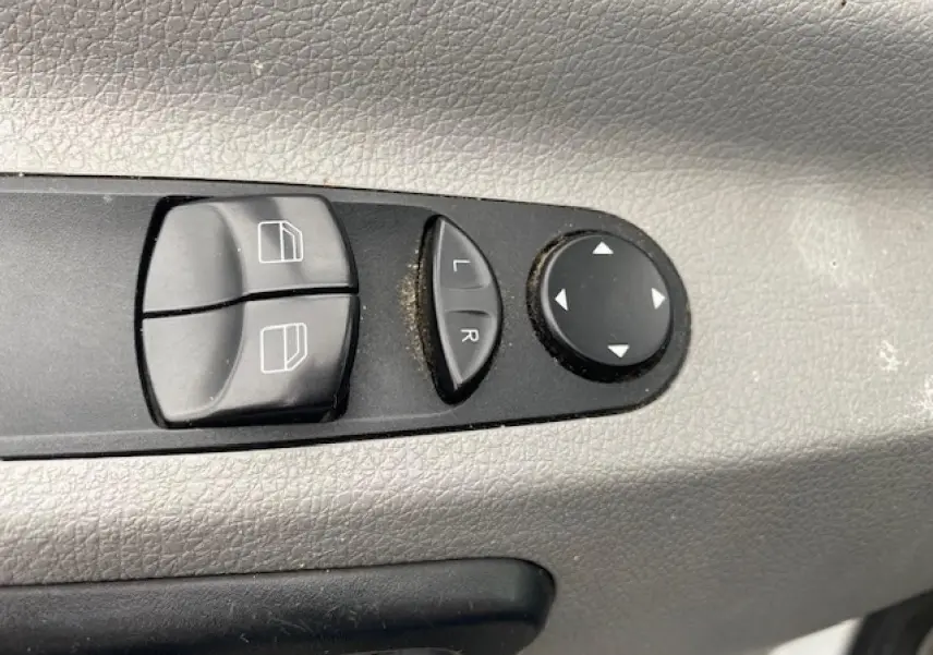 Gros plan sur les commandes électriques des vitres et des rétroviseurs du Mercedes Sprinter blanc, côté conducteur.