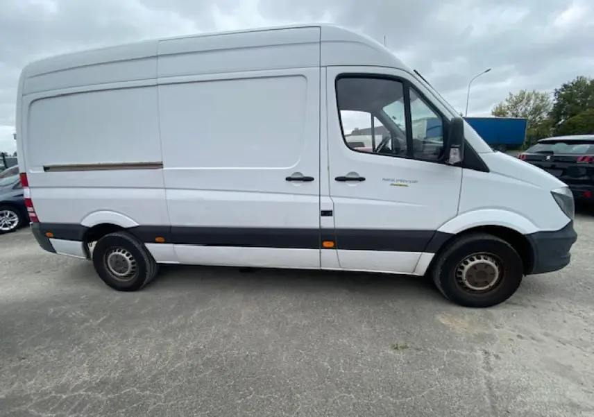 Vue latérale gauche d'un fourgon Mercedes Sprinter blanc de 2015 avec bande noire et jantes acier simples.