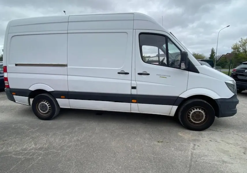 Vue de profil côté gauche d’un Mercedes Sprinter Fourgon blanc de 2015 avec bande noire et feux latéraux orange.