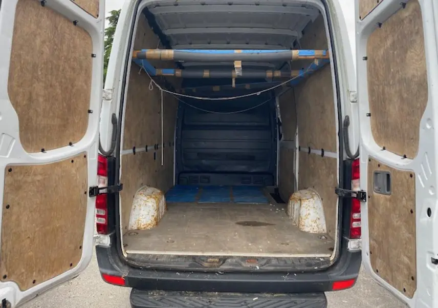 Vue arrière ouverte du Mercedes Sprinter blanc 2015, montrant l'intérieur utilitaire avec aménagements en bois et structure métallique.