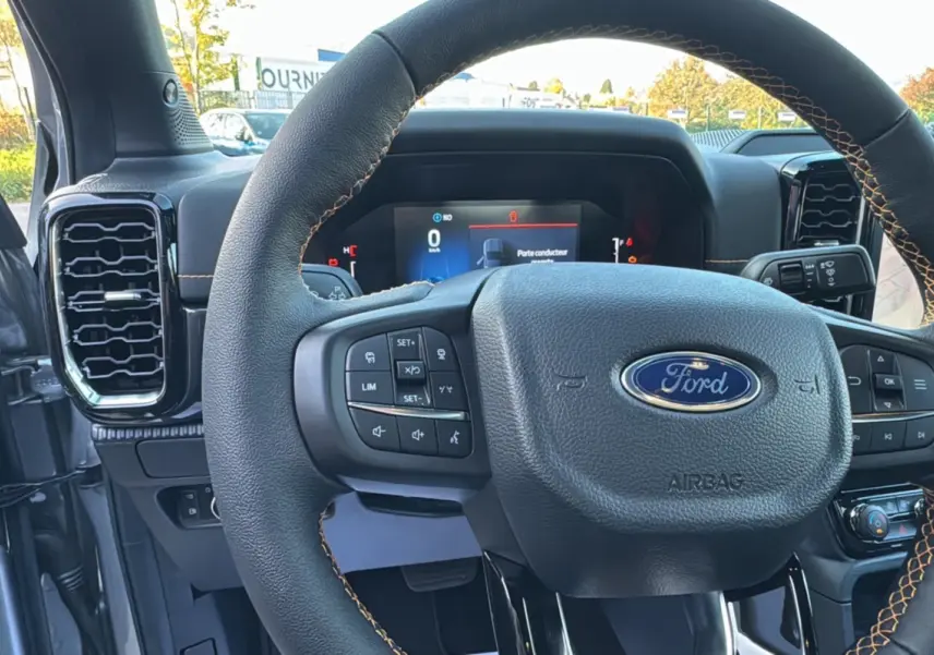 Vue rapprochée du volant cuir noir avec surpiqûres marron du Ford Ranger PHEV 281 Wildtrak, tableau de bord numérique visible.