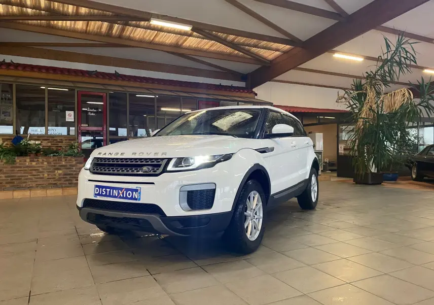 Range Rover Evoque blanc vu en 3/4 avant droit dans un showroom avec phares allumés.