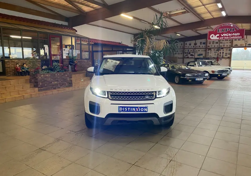 Vue avant d'un Range Rover Evoque blanc 2016 avec phares allumés dans un showroom intérieur.