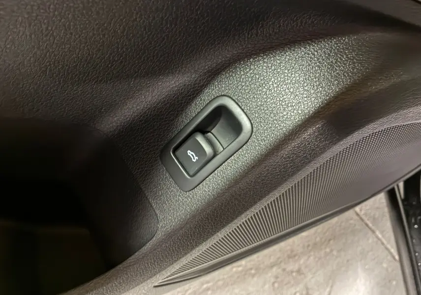Bouton d'ouverture du coffre intégré dans la garniture intérieure noire de la porte d'un Audi Q2 35 TFSI 2023.