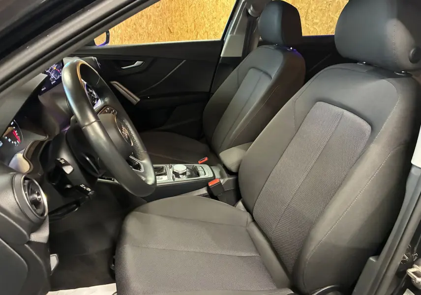 Vue intérieure côté conducteur de l'Audi Q2 35 TFSI S-Line 2023 avec sièges tissu noir et volant multifonction.