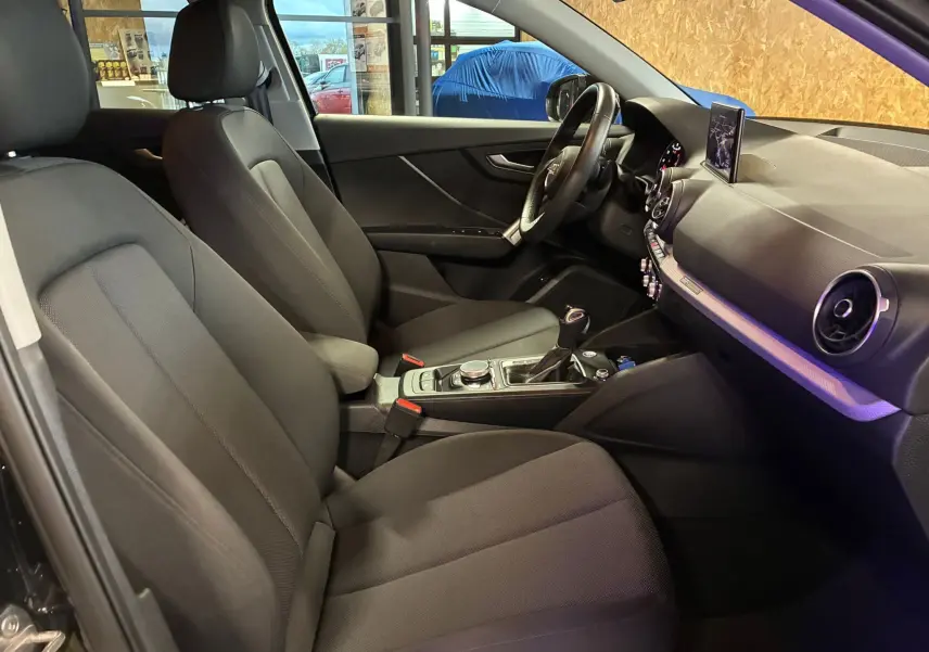 Intérieur noir de l'Audi Q2 35 TFSI 2023 vu côté conducteur, avec tableau de bord moderne et écran central déployé.