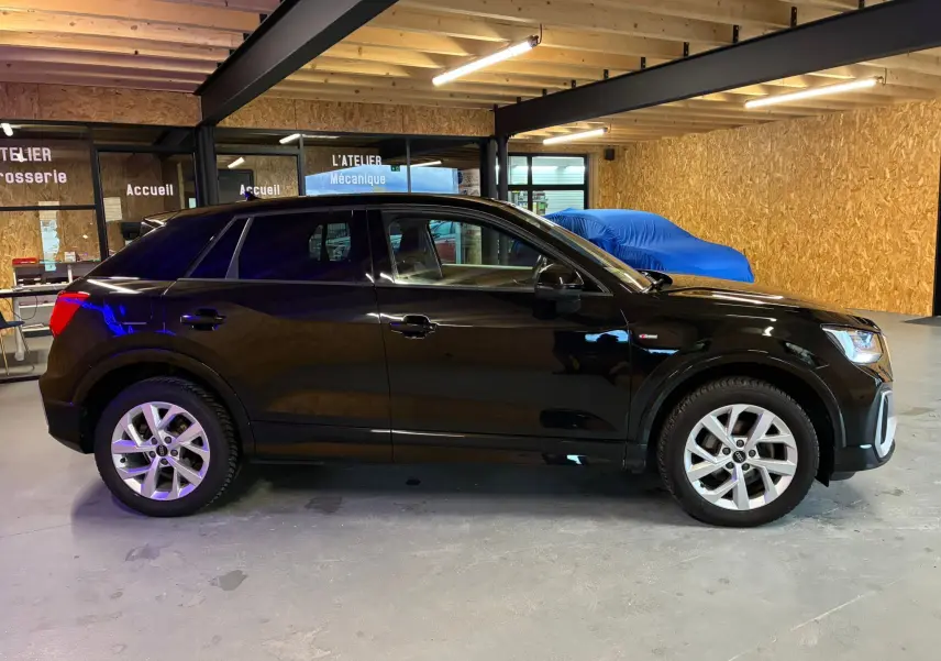 Audi Q2 noir vue de profil côté gauche dans un garage, soulignant ses jantes alliage et finition S-Line.