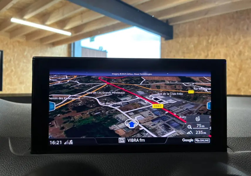 Écran GPS de l'Audi Q2 noir 2023 montrant une carte en 3D avec itinéraire en rouge, intérieur visible en arrière-plan.
