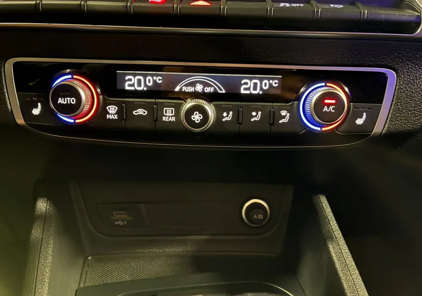 Panneau de commande de climatisation digitale de l'Audi Q2 35 TFSI noir, avec réglages à 20°C et boutons rétroéclairés rouge et bleu.