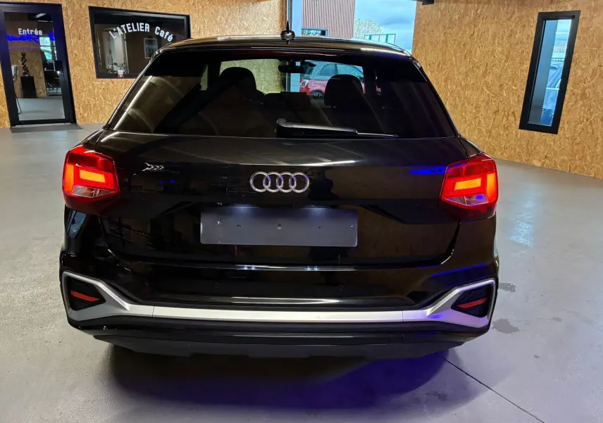 Vue arrière d'un Audi Q2 noir 2023 avec feux allumés dans un garage au sol gris.