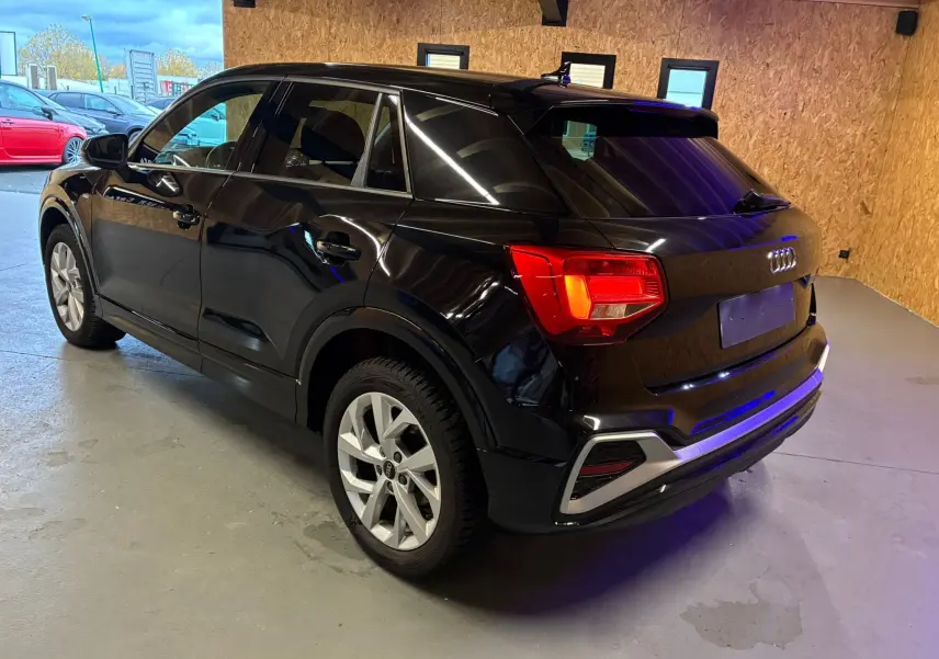 Audi Q2 noir vue 3/4 arrière droit dans un garage, avec feux arrière allumés et jantes argentées.