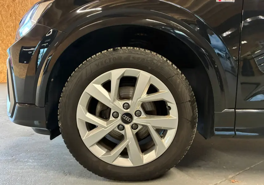 Gros plan sur la roue avant gauche d'un Audi Q2 noir 35 TFSI S-Line avec jante argentée et logo Audi central.