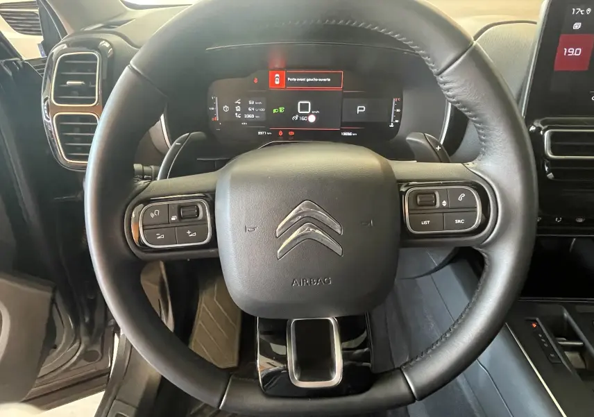 Vue rapprochée du volant en cuir noir du Citroën C5 Aircross Hybride 2025 avec commandes intégrées et tableau de bord digital.