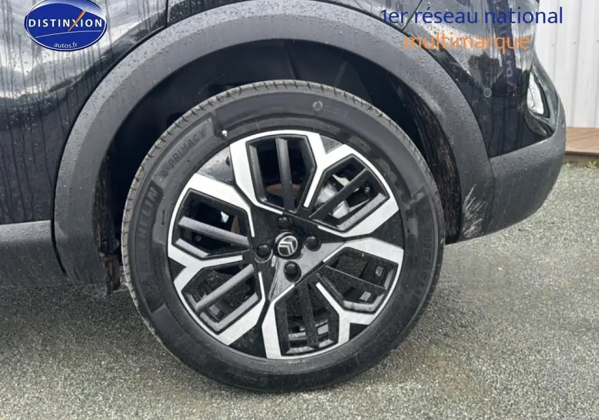 Gros plan sur la roue avant droite noire d'une Citroën C4 1.2 hybride 2025 avec jante alu bicolore.