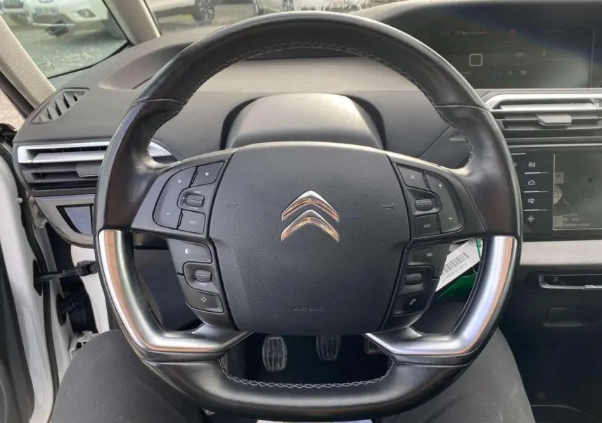 Vue centrée sur le volant cuir noir du Citroën Grand C4 Picasso blanc, avec commandes intégrées et tableau de bord numérique.