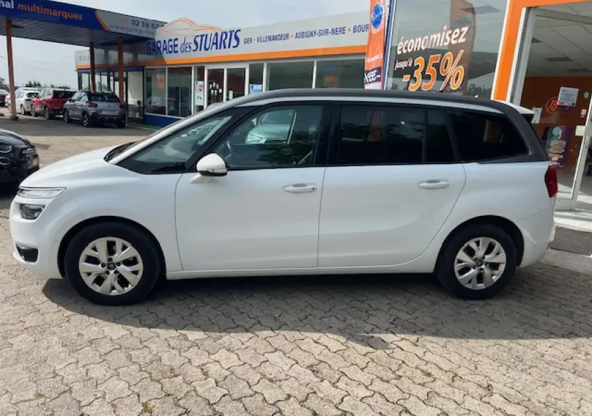 Vue de profil côté gauche d'un Citroën Grand C4 Picasso blanc stationné devant un garage avec vitres latérales surteintées.