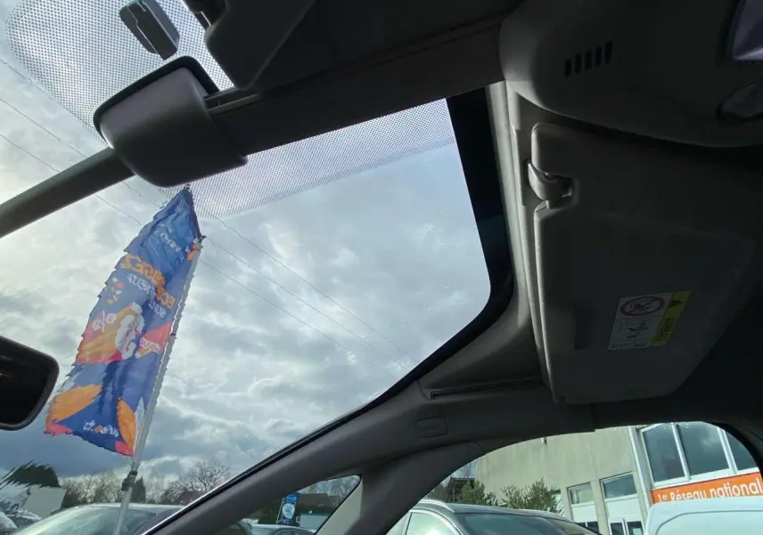 Vue intérieure du toit ouvrant panoramique du Citroën Grand C4 Picasso blanc, avec pare-soleil et ciel nuageux visible.