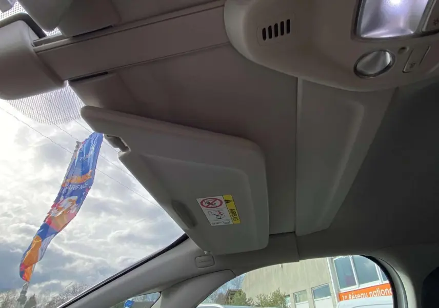 Intérieur du Citroën Grand C4 Picasso 2015, vue du pare-soleil conducteur beige avec ciel nuageux visible.