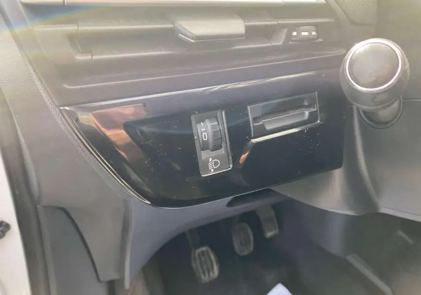 Détail intérieur côté conducteur du tableau de bord du Citroën Grand C4 Picasso blanc, avec commande de réglage des phares et levier de boîte manuelle.