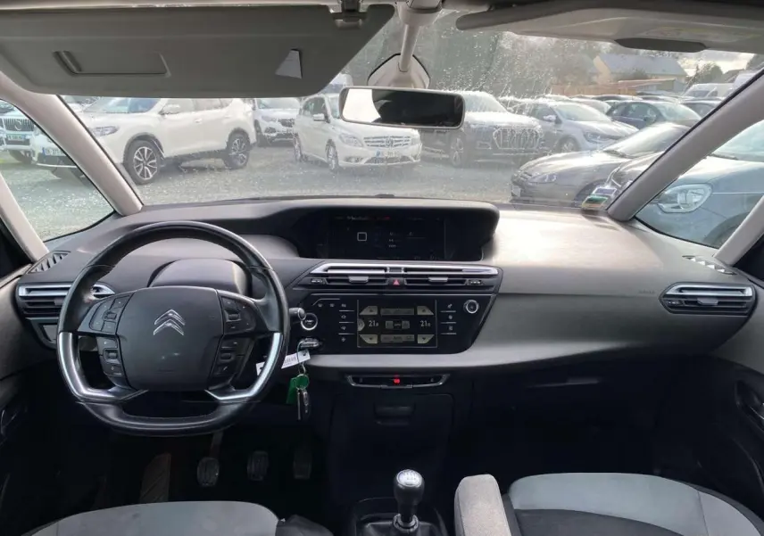 Vue intérieure frontale du tableau de bord et volant cuir noir du Citroën Grand C4 Picasso blanc, avec écran tactile et boîte manuelle.
