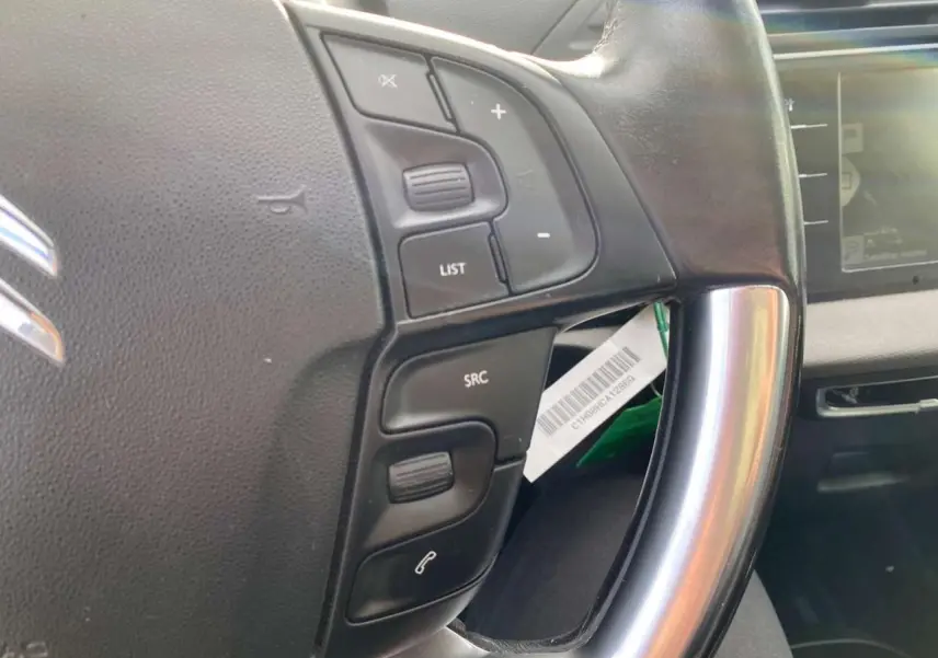 Gros plan sur le volant cuir noir du Citroën Grand C4 Picasso 2015, avec commandes audio et écran tactile en arrière-plan.