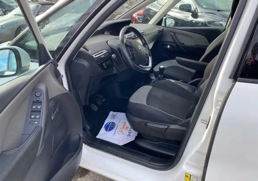 Vue intérieure côté conducteur d'un Citroën Grand C4 Picasso blanc, montrant sièges tissu bicolore et volant multifonction.